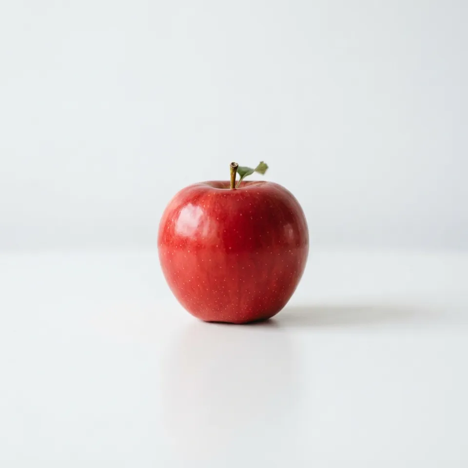A single red apple on a white table against a pale background