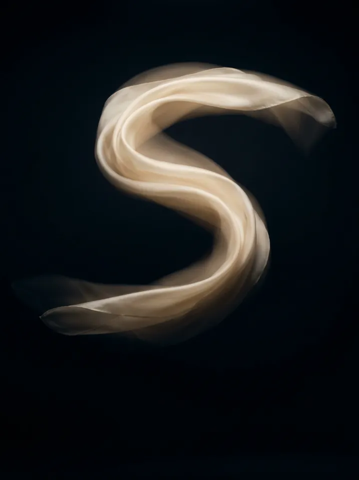 A cream silk scarf caught mid-air as a soft S-shaped motion trail against a black backdrop