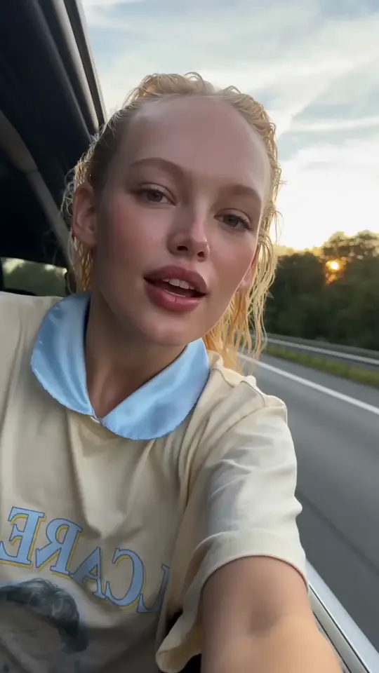 A woman filming herself in a car at golden hour, a still from a clip made in AIGE